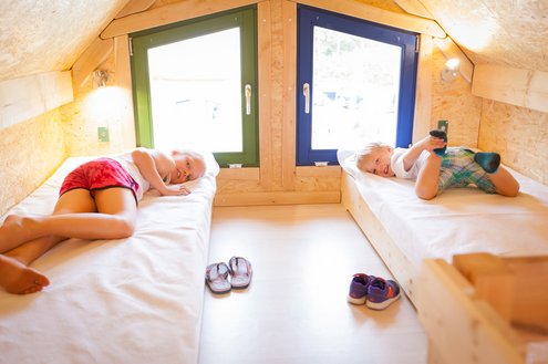 In einem aus Holz gebauten Märchenhaus liegen zwei Kinder in nebeneinander angebrachten Kinderbetten im Obergeschoss.
