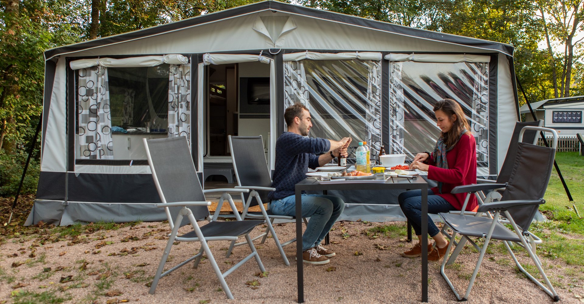 Ein Mann und eine Frau sitzen vor ihrem Wohnwagen an einem Tisch und essen etwas.