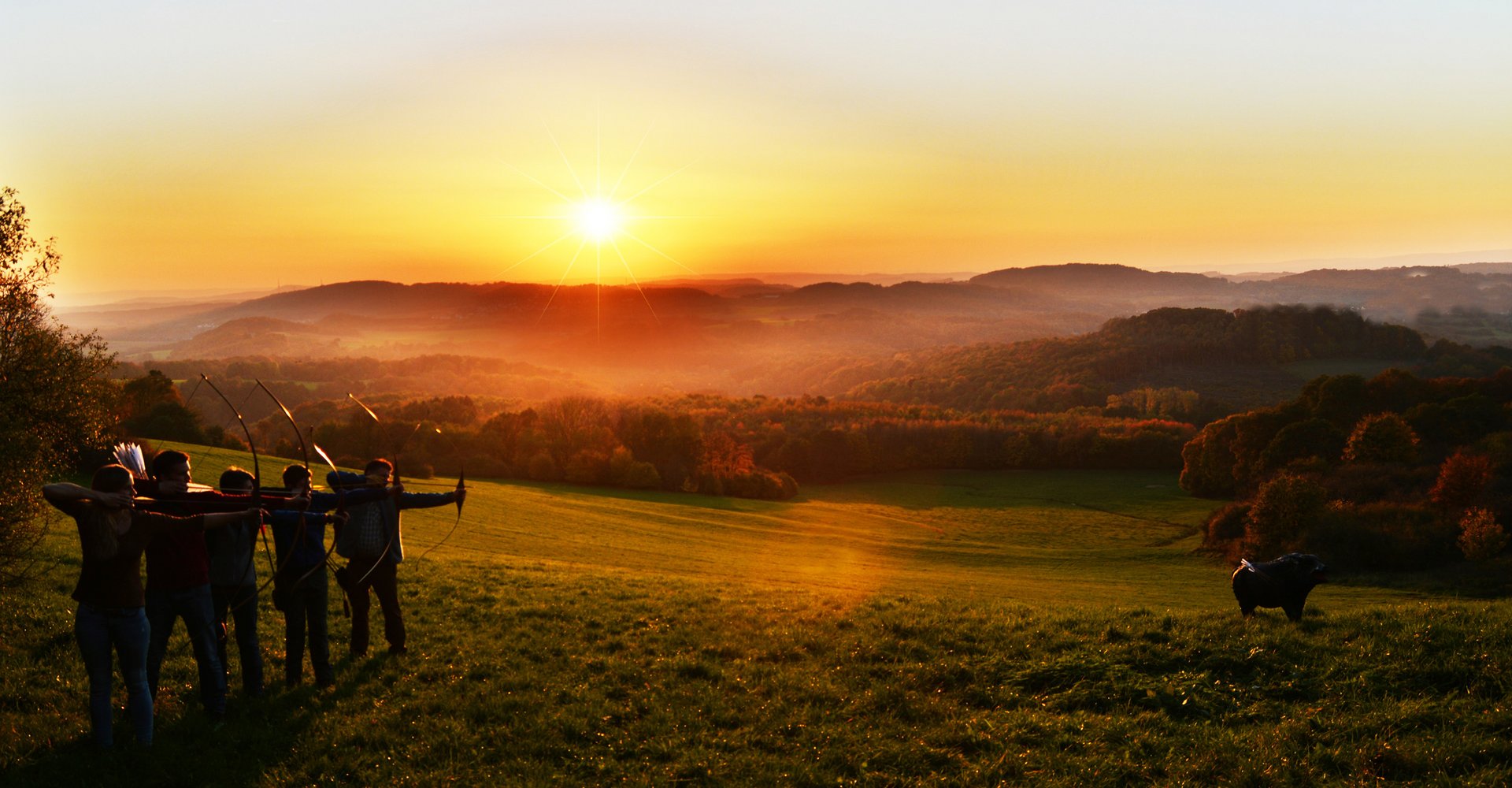 Mehrere Personen schießen bei Sonnenuntergang mit ihren Pfeilen und Bögen auf ein 3D-Ziel.