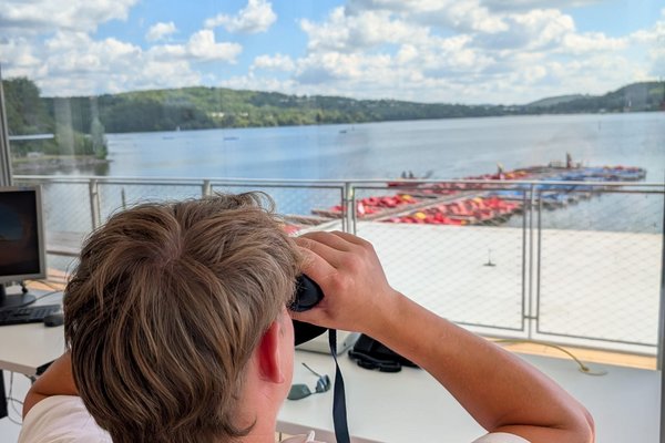 Ein Mitarbeiter der Rettungswache schaut durch ein Fernglas und beobachtet das Treiben auf dem Bostalsee.