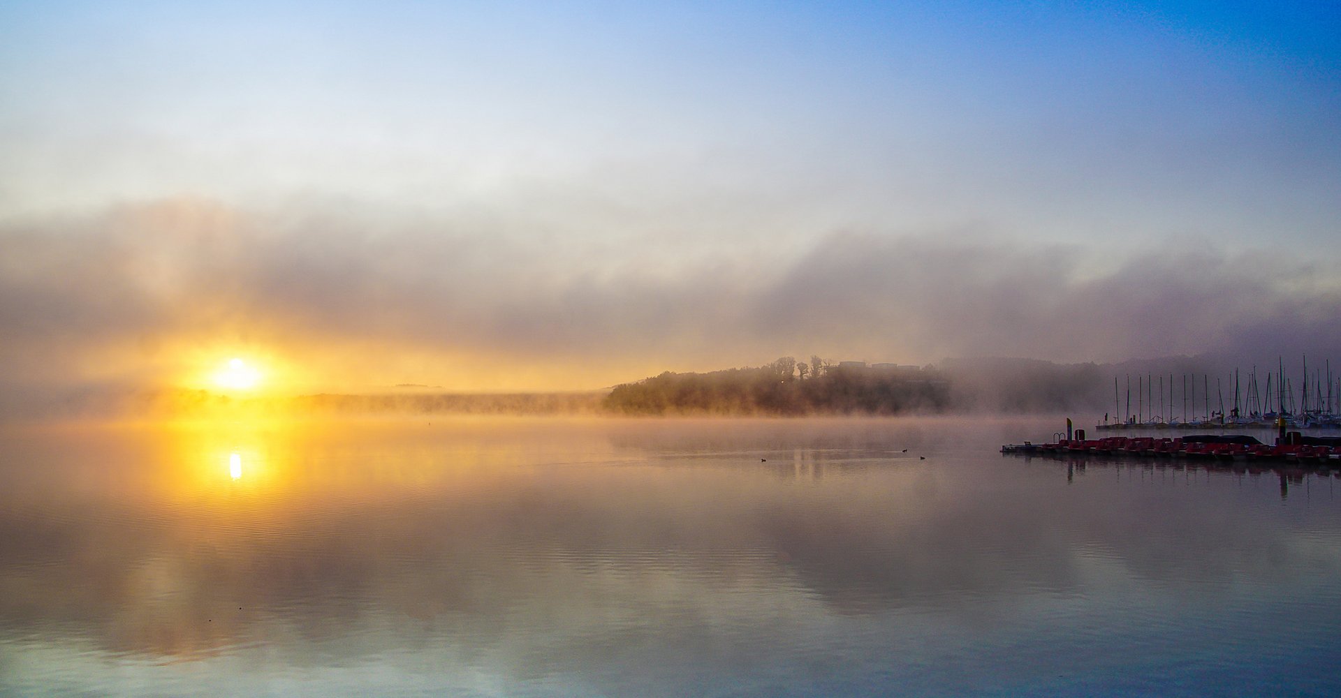 Der Bostalsee ist in Nebel gehüllt. Die Sonne geht gerade auf und verströmt ihr goldenes Licht.